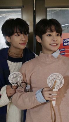 two young men standing next to each other in front of a door holding wind chimes