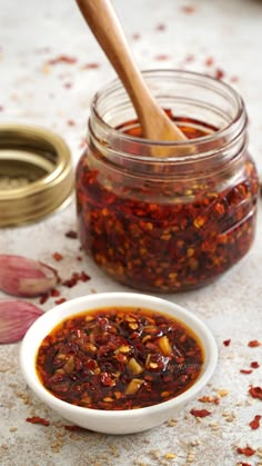 homemade chili oil in a small white bowl next to a wooden spoon and garlic flakes