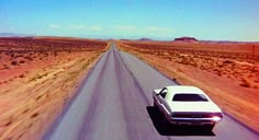 an old car driving down the road in the middle of the desert with no cars on it