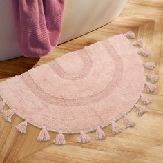 a pink rug with tassels is on the floor next to a bathtub