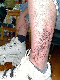 a person with a tattoo on their leg sitting next to a white sneaker shoe