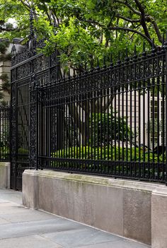 an iron fence is shown in front of a building with trees on the other side