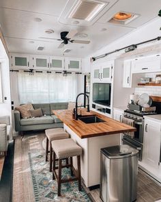 a kitchen and living room area in a mobile home with white cabinets, wood counter tops, stainless steel appliances and an island