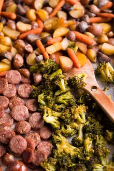 sausage, broccoli and carrots on a sheet with a wooden spoon next to them