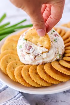 a cracker being dipped into a bowl of dip surrounded by crackers on a white plate