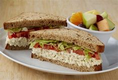 a cut in half sandwich sitting on top of a plate next to a bowl of fruit