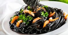 a plate of pasta with shrimp and parsley on top, served with a fork