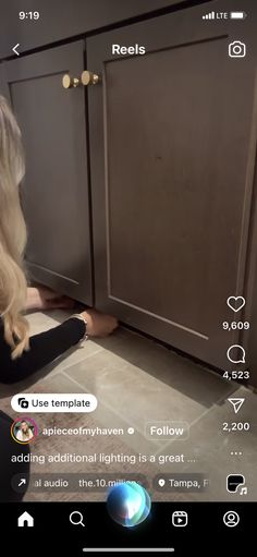 a woman sitting on the floor in front of a kitchen cabinet with an appliance