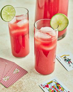 two glasses filled with watermelon and limeade next to playing cards on a table