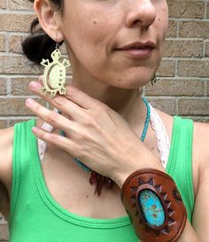 a woman wearing a green tank top and brown leather bracelet with an animal charm on it