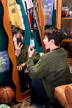 two young men sitting in front of a mirror looking at their cell phones and taking pictures