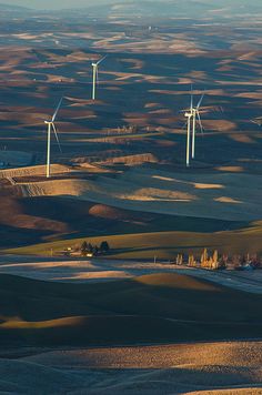 an aerial view of several wind turbines in the distance, with fields and trees on either side