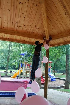 a man standing on top of a wooden roof next to a pink playground area filled with toys