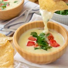 a person dipping tortilla chips into a bowl of quesadilla soup