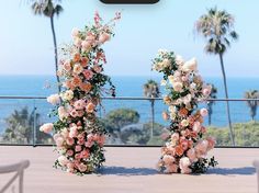 two tall floral arrangements sitting on top of a wooden floor next to the ocean and palm trees