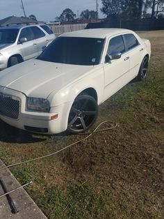 a white car is parked in the grass next to two other cars on the side of the road