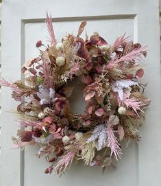 a wreath hanging on the side of a white door with pink and green flowers in it