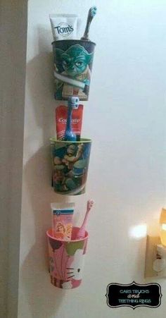 three cups are hanging on the wall with toothbrushes and toothpaste