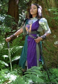 a woman dressed as a knight standing in the woods