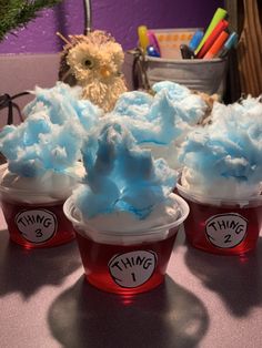 three plastic cups filled with blue and white frosting on top of a table next to a teddy bear