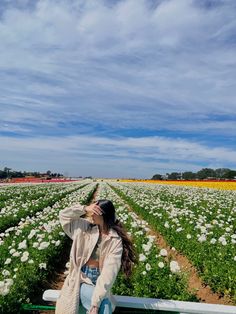 a woman sitting on a bench in the middle of a field with lots of flowers