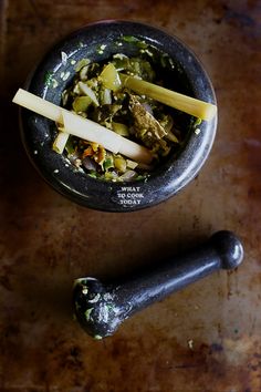 a bowl filled with food sitting on top of a wooden table next to two metal spoons