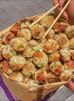 a person holding a paper bag filled with dumplings and chopsticks in it