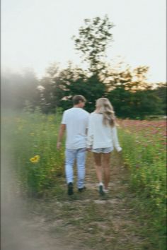 a man and woman walking down a dirt road in the middle of a flower field