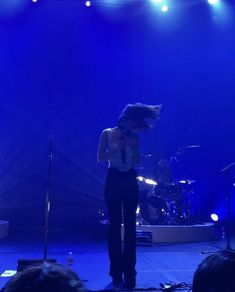 a woman standing on top of a stage with microphones in front of blue lights