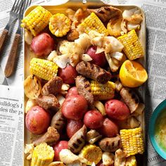 a tray filled with meat, potatoes and corn on the cob