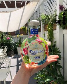 a hand holding a bottle of donjuto in front of a patio with potted plants