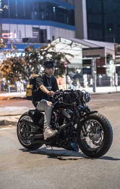 a man riding on the back of a motorcycle down a street next to tall buildings