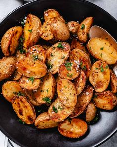 cooked potatoes with parmesan cheese and herbs in a black bowl on a white table