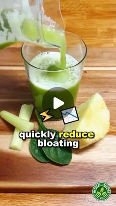 a glass filled with green liquid sitting on top of a wooden table next to sliced apples