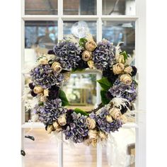 a wreath with purple and white flowers is hanging on a window sill in front of a glass door