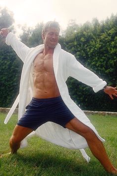 a man in shorts and a white robe is doing yoga on the grass with his arms stretched out