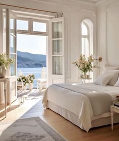 a bedroom with white walls and windows overlooking the water is furnished with an elegant bed