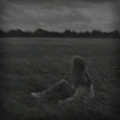 black and white photograph of a woman sitting in the grass with an overcast sky behind her