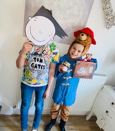 two children in costumes standing next to each other holding up a cardboard cut out of a boy and girl