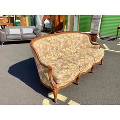 an old couch sitting on top of a parking lot next to a green building with lots of furniture in it