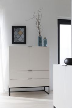 a white dresser with two vases on top of it next to a black and white cabinet