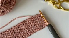 a pair of scissors next to a pink crocheted piece of cloth and thread