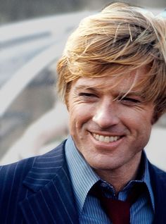 a close up of a person wearing a suit and tie with blonde hair smiling at the camera