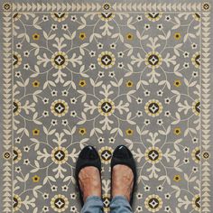 a person wearing black shoes standing in front of a floral pattern on the floor with their feet up