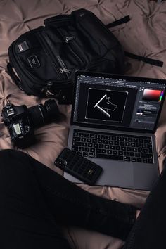 an open laptop computer sitting on top of a bed next to a camera and cell phone