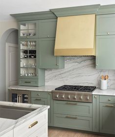 a kitchen with green cabinets and marble counter tops, an oven hood over the stove