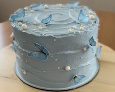 a blue cake with white frosting and butterflies on it sitting on a wooden table