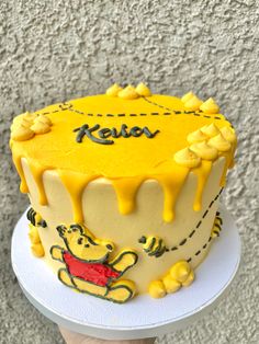 a cake with yellow frosting and winnie the pooh on top is being held up by someone's hand