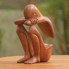 a wooden statue of a sitting rabbit holding its head in his hands on a table