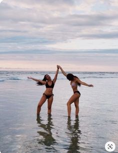 two women in black bikinis are standing in the water and holding their arms up